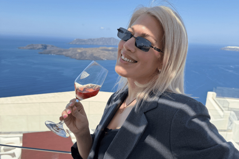 Santorini private wine tour guest holding a glass of rosé wine with panoramic caldera and volcanic islands view in daylight