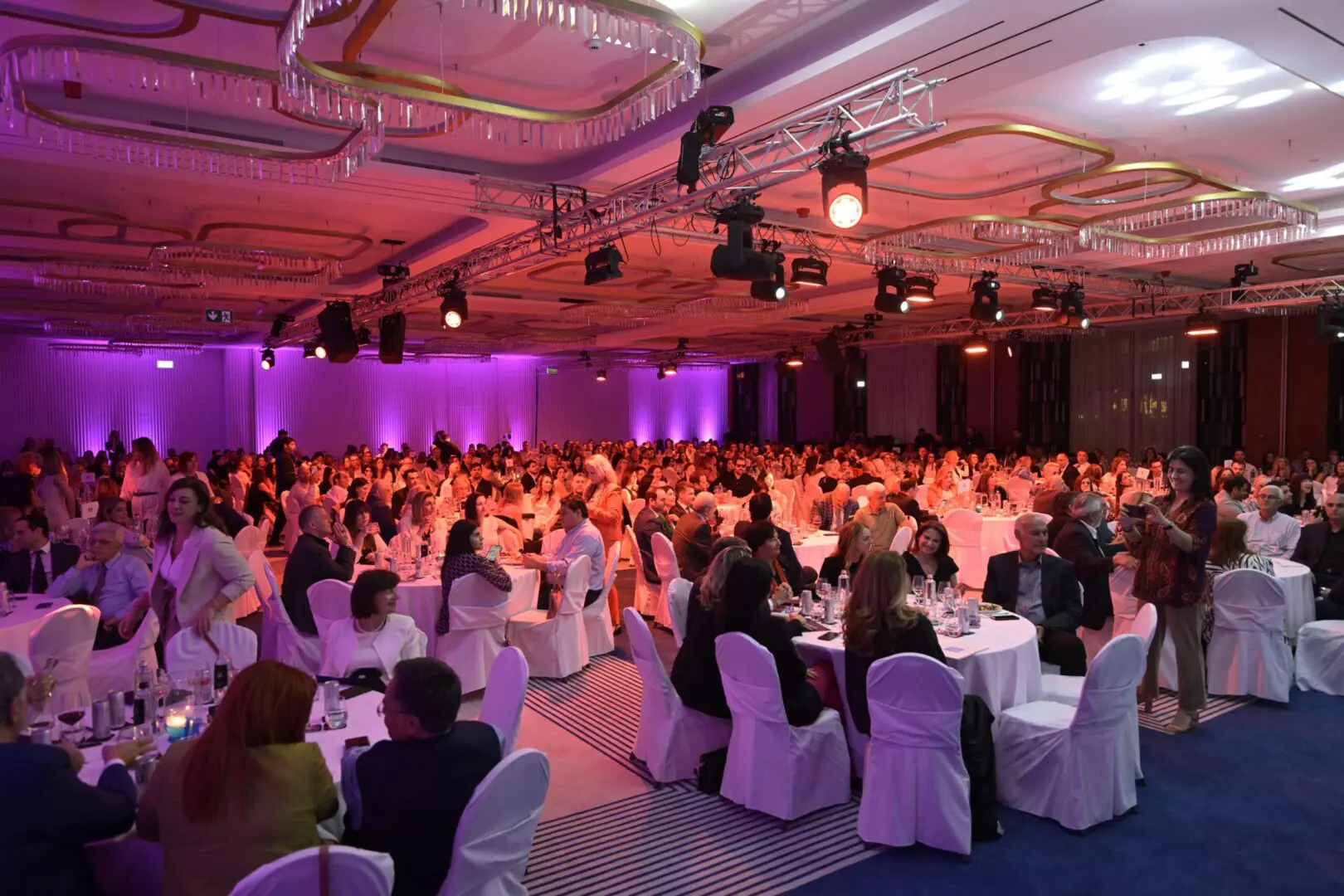 A large ballroom filled with people at tables, lit with pink and red lighting for an awards ceremony.