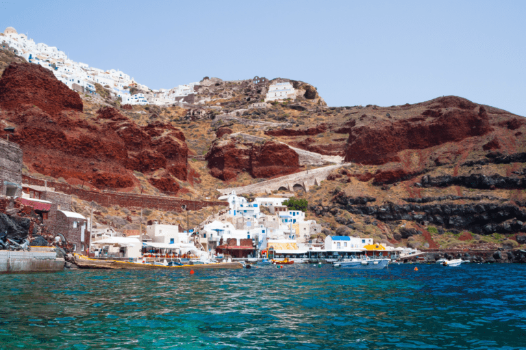 Ammoudi Bay village seen from the sea with red cliffs and turquoise waters