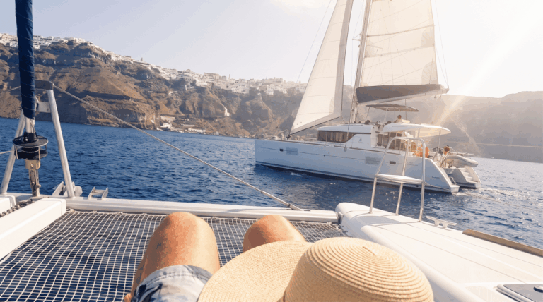 Catamaran sailing past the Oia cliffs in the Santorini caldera, seen from the bow net of a sailing cruise