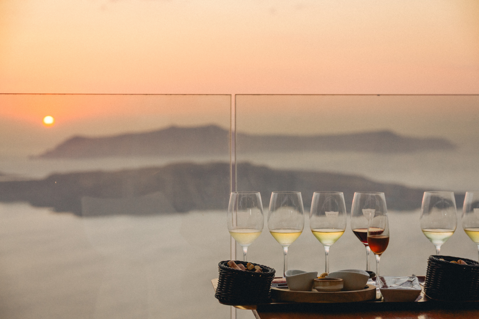 Santorini Sunset Wine Tasting with Caldera Views Multiple wine glasses filled with white and rosé wine on a table overlooking the Santorini caldera at sunset