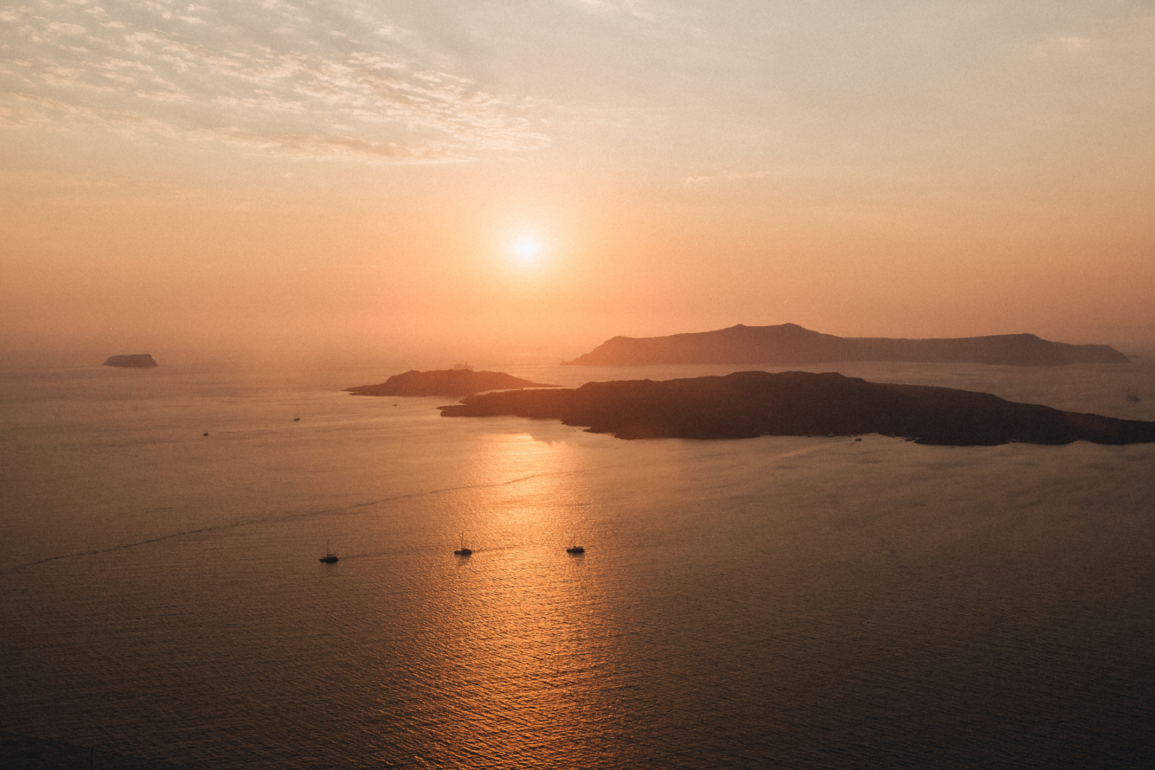 Santorini Caldera at Golden Hour Aerial view of the Santorini caldera with sailboats on the sea and volcanic islands silhouetted against a golden sunset sky