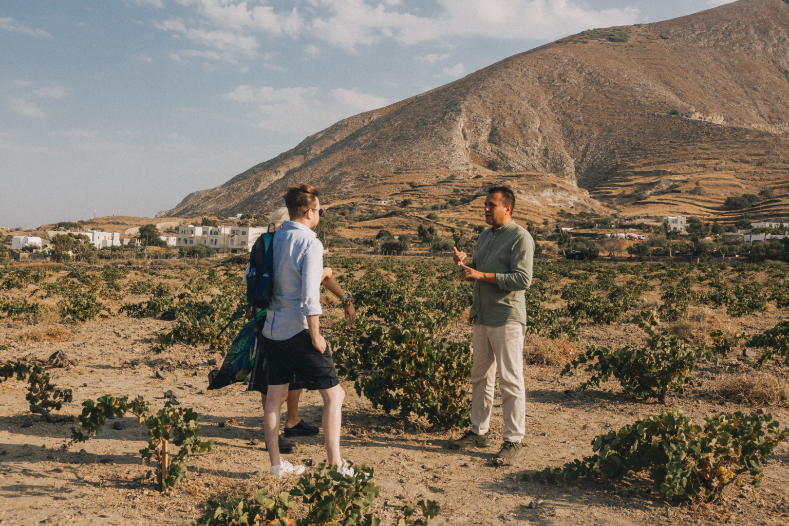 Private Vineyard Walk in Santorini our guide explaining Santorini viticulture to two guests standing in a vineyard with basket-trained vines and a volcanic hillside in the background