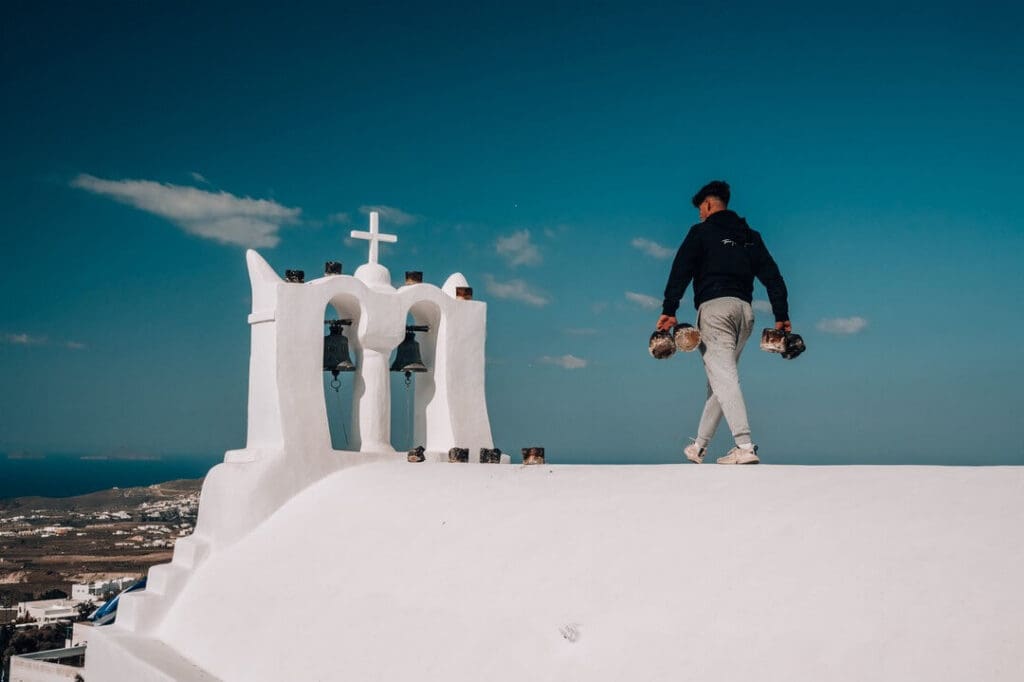 A person carries used Easter candles away from a whitewashed church bell tower in Santorini, Greece.