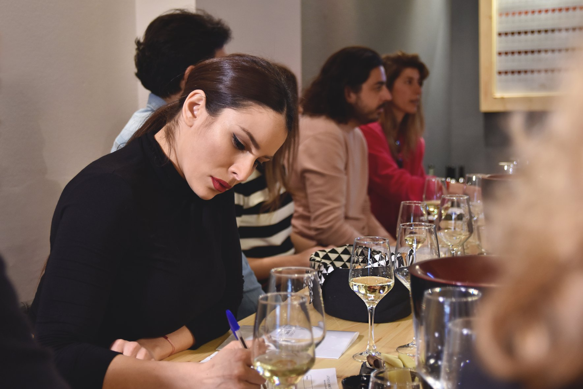 Wine Tasting in Athens A person with dark hair is seated at a table, writing in a notebook while tasting wine, at an Athens wine tasting experience.