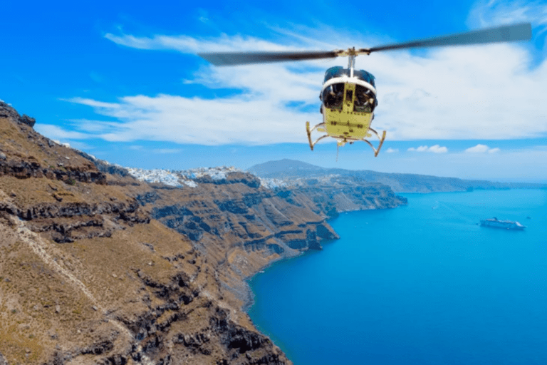 A helicopter flying above a coastal caldera, with rugged cliffs on one side and clear blue sea stretching below.