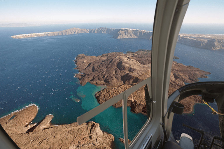 View from inside a helicopter over Santorini, looking out across the volcanic islands and turquoise and deep blue waters of the Aegean Sea.