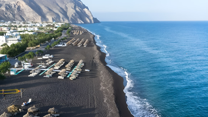 Black sand beach in Santorini with sunbeds and umbrellas along the coastline, one of the top beach activities to do in Santorini during vacation.