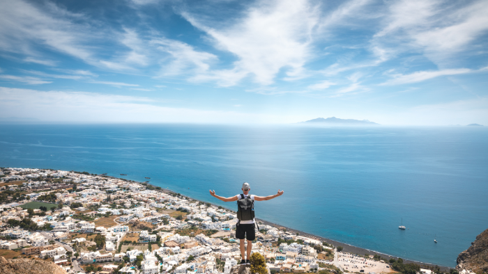 Traveler overlooking Santorini caldera and whitewashed villages from a scenic viewpoint, one of the best things to do in Santorini.