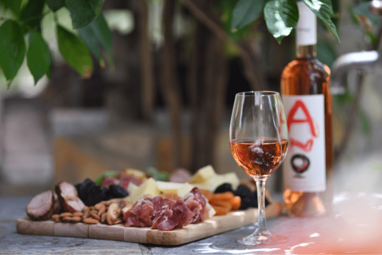 Glass of rosé wine on a wooden table beside a Cretan tasting board with cured meats, cheese, nuts, and olives at Anoskeli Winery, Crete.