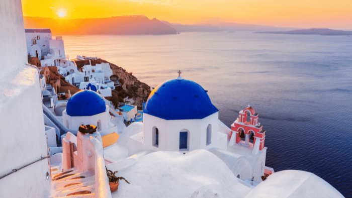 Santorini blue-domed churches at sunset overlooking the caldera, an iconic finale for an Athens Crete Santorini itinerary.