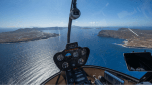 View from inside a helicopter cockpit overlooking the sea and coastal islands during flight, with flight instruments visible in the foreground.