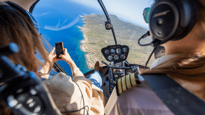 Helicopter flight over the coastline of Santorini with passengers enjoying aerial sea views and taking photos