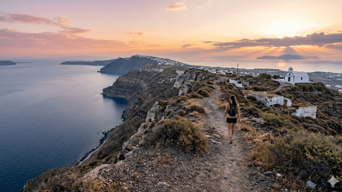 Woman hiking the Fira to Oia trail at sunset in Santorini, with the caldera and whitewashed villages in the background