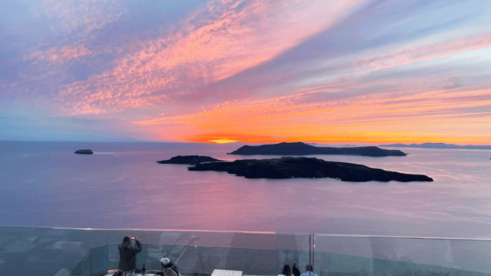 Dramatic orange and pink sunset over the Santorini caldera islands, viewed from a cliffside terrace in autumn