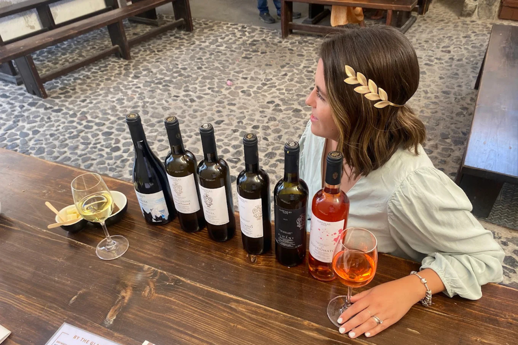 Wine Tasting at Gavalas Winery, Santorini Wine tasting setup at Gavalas Winery in Santorini with several wine bottles lined up on a wooden table alongside wine glasses during a tasting session.