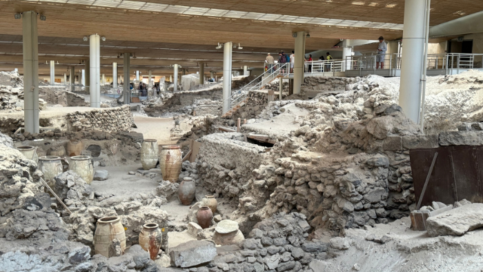 Archaeological ruins of Ancient Akrotiri in Santorini, with preserved structures, pottery vessels, and walkways inside the excavation site