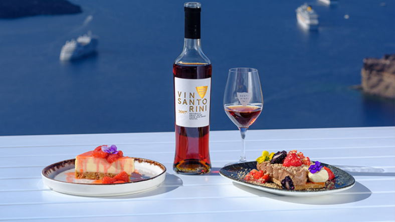 Vinsanto Santorini wine poured in a glass alongside Greek desserts with caldera sea view
