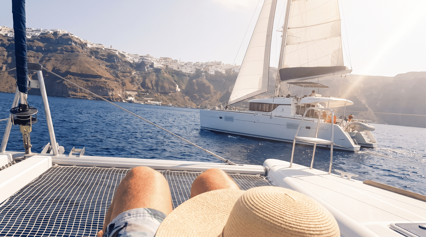 Catamaran sailing past the Oia cliffs in the Santorini caldera, seen from the bow net of a sailing cruise