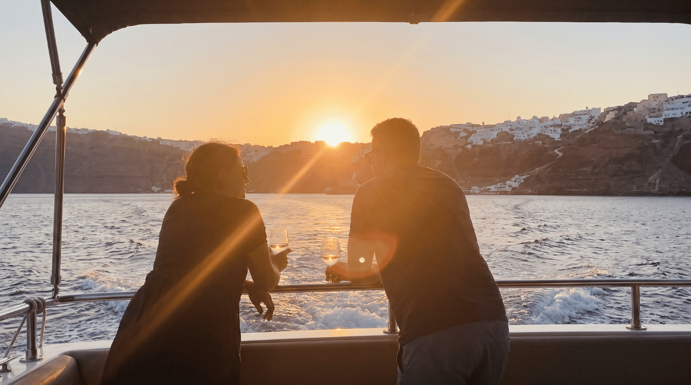 Couple watching the sunset over the Santorini caldera with wine glasses from the deck of a sailing cruise